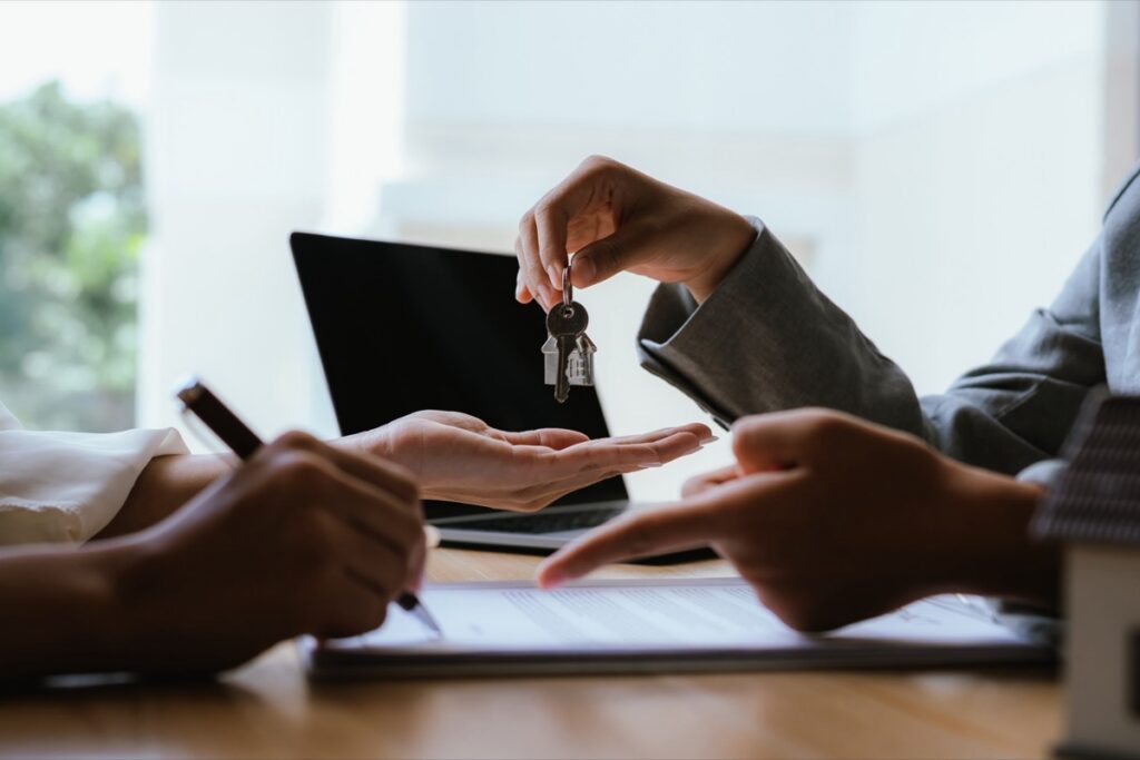 Agent handing house keys to a client across a desk at closing